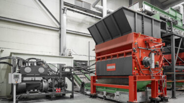 A large orange shredder with a powerful drive system at a recycling plant