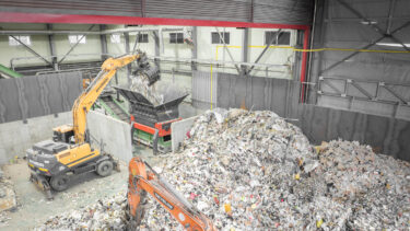 Drohnenaufnahme von Müllbergen die mit zwei Baggern in einen orangenen Shredder gegeben werden