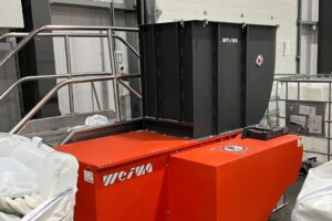 An orange shredder in a production hall between big bags filled with plastic production waste