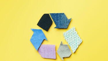 Reuse, reduce, recycle concept background. Recycle symbol made from old clothing on yellow background. Top view or flat lay.