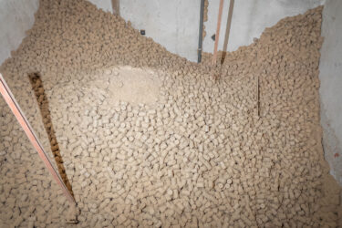 Großer Vorrat an hellen Holzbriketts in einem Brennstofflager, teilweise mit feinem Holzstaub bedeckt