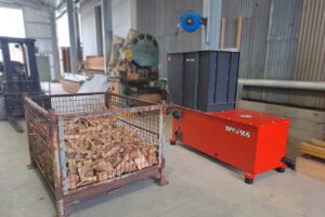 An orange shredder next to a mesh crate filled with wood scraps in a warehouse.