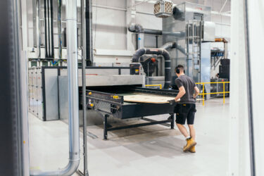 Bulky production waste is fed into a WEIMA horizontal shredder. The shredder is located in a hall; a man can be seen working on the machine.