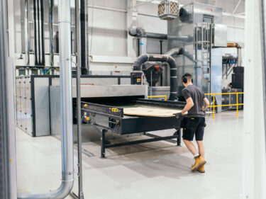 Sperrige Produktionsreste werden in einen Horizontal-Zerkleinerer von WEIMA gegeben. Der Shredder und steht in einer Halle, man sieht einen Mann der an der Maschine arbeitet.