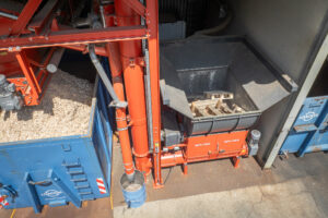 Drone shot of an orange wood shredder in operation, featuring a conveyor system and a container filled with wood chips alongside it.