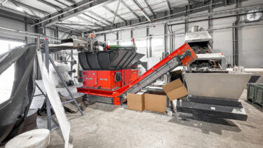 A WEIMA WLK 1500 with a roller feed in a workshop. This is followed by a conveyor belt and onward transport to an extruder.