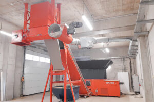 An orange shredder in a warehouse with an attached screw conveyor.
